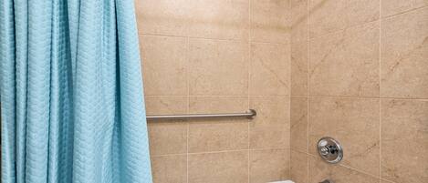 A bathroom with beige tiles, a white bathtub, a showerhead, and a grab bar.