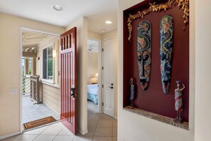 Un couloir avec une porte rouge, une petite statue et un mur décoratif orné de masques.