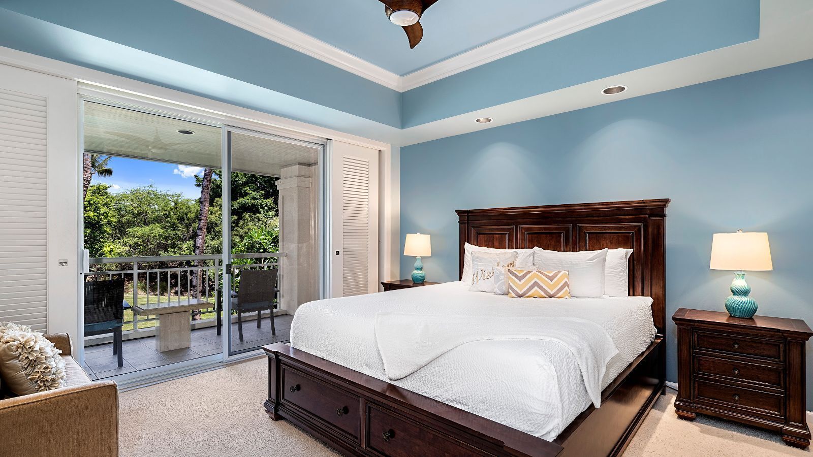 A bedroom with a large bed, two bedside tables, a chair, and a sliding glass door leading to a balcony.