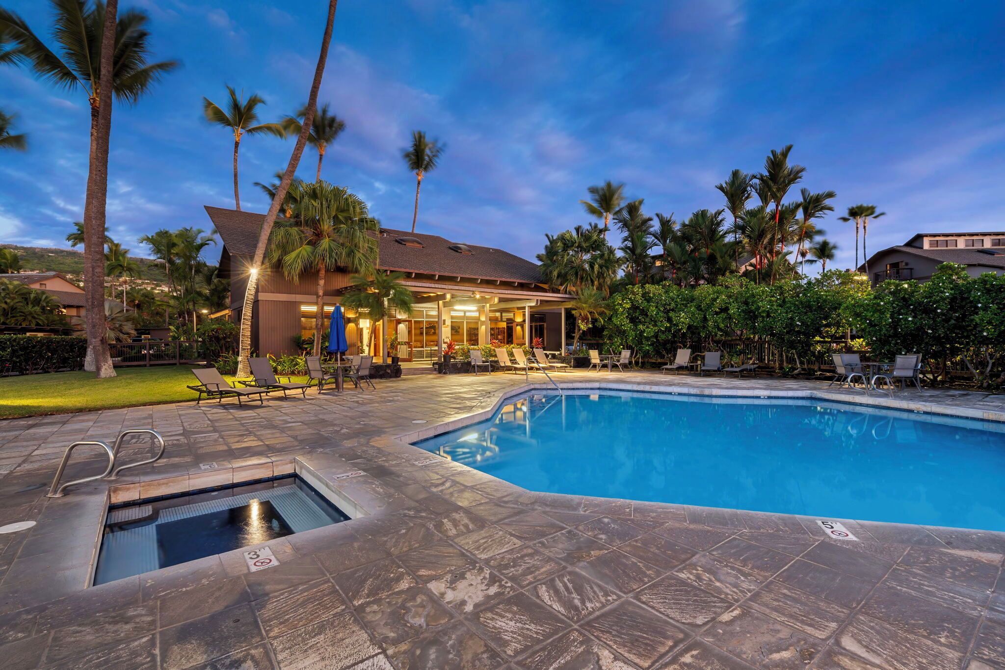 A swimming pool with a hot tub, lounge chairs, and palm trees.