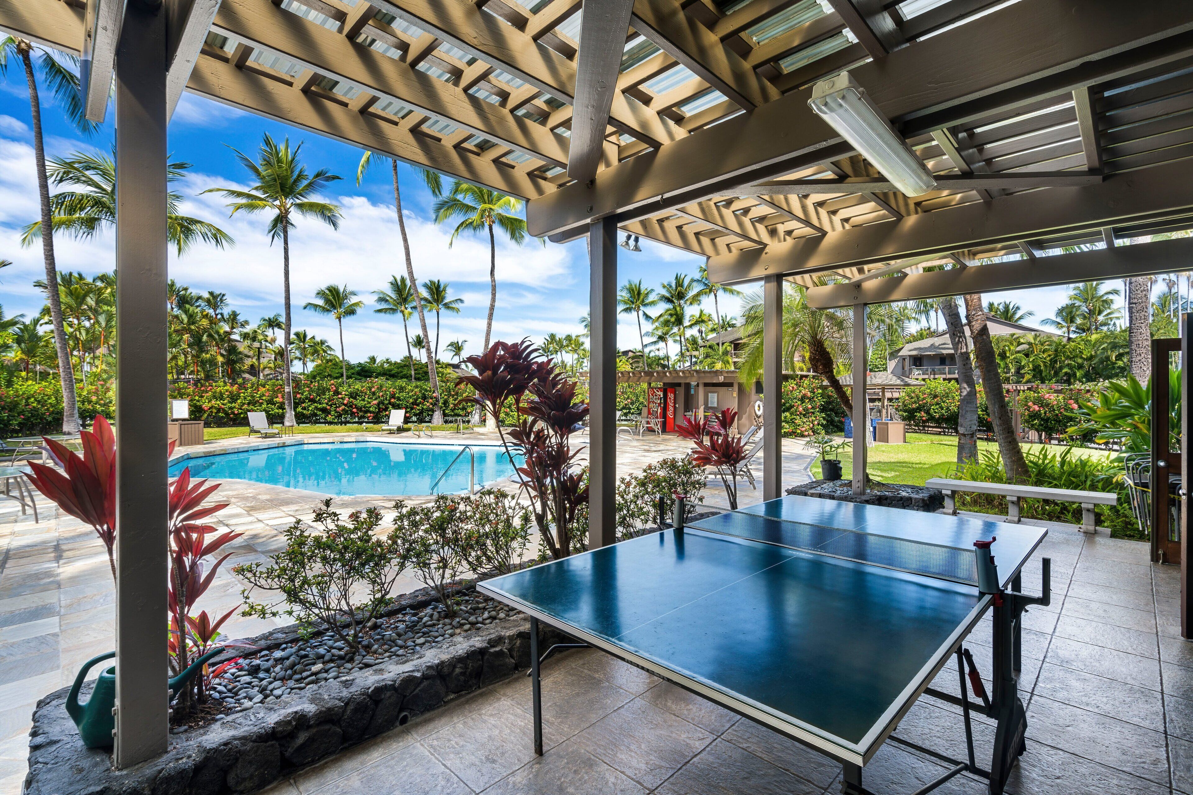 A ping pong table in an outdoor area with a pool and palm trees in the background.