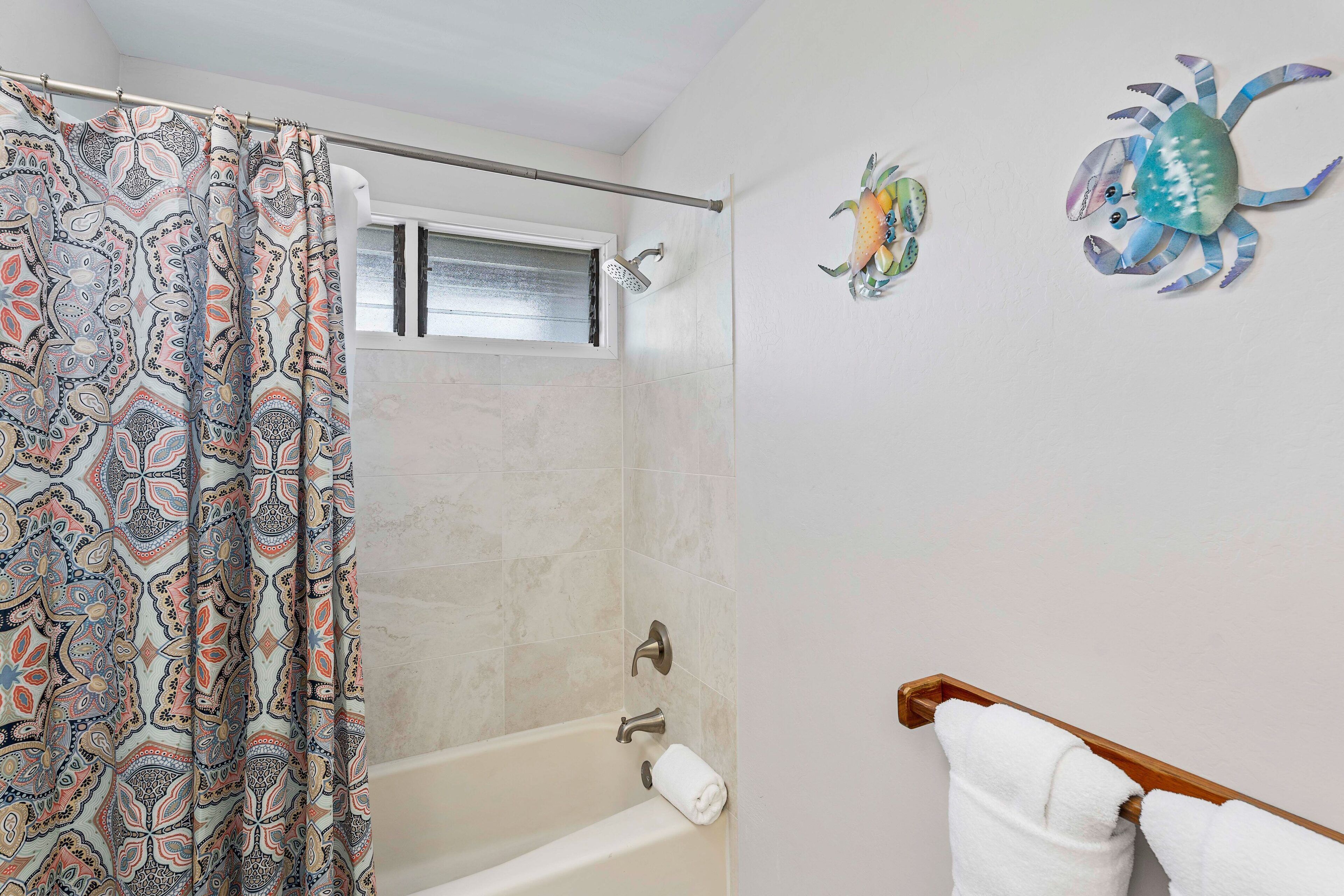 A bathroom with a patterned shower curtain, a bathtub, a towel rack, and two decorative crab wall art pieces.