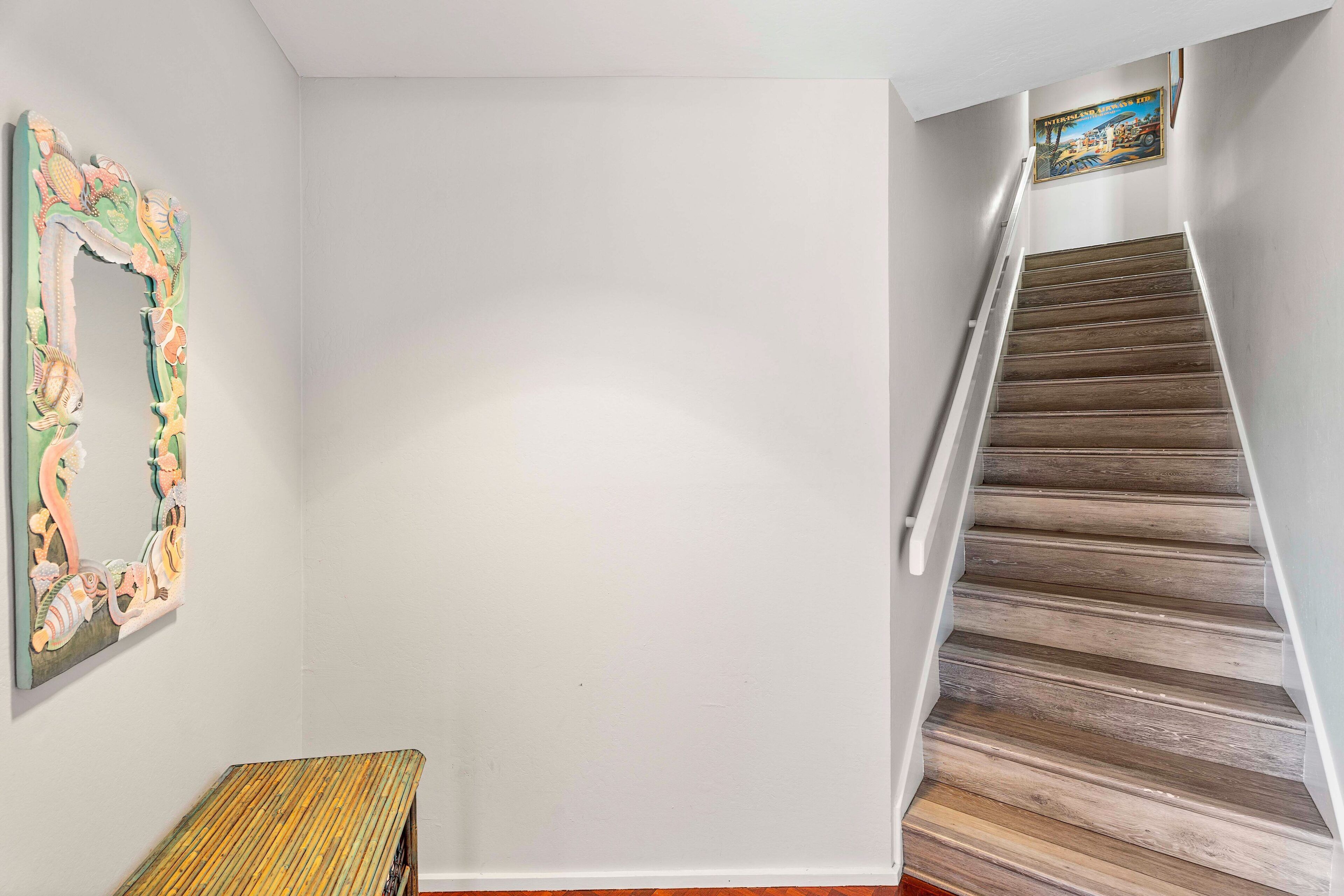 A staircase with wooden steps and white railings, a colorful abstract painting on the wall, and a bench at the bottom.