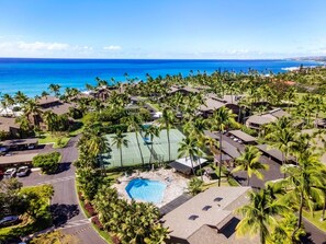 An aerial view of a resort with a swimming pool, tennis courts, and a view of the ocean.