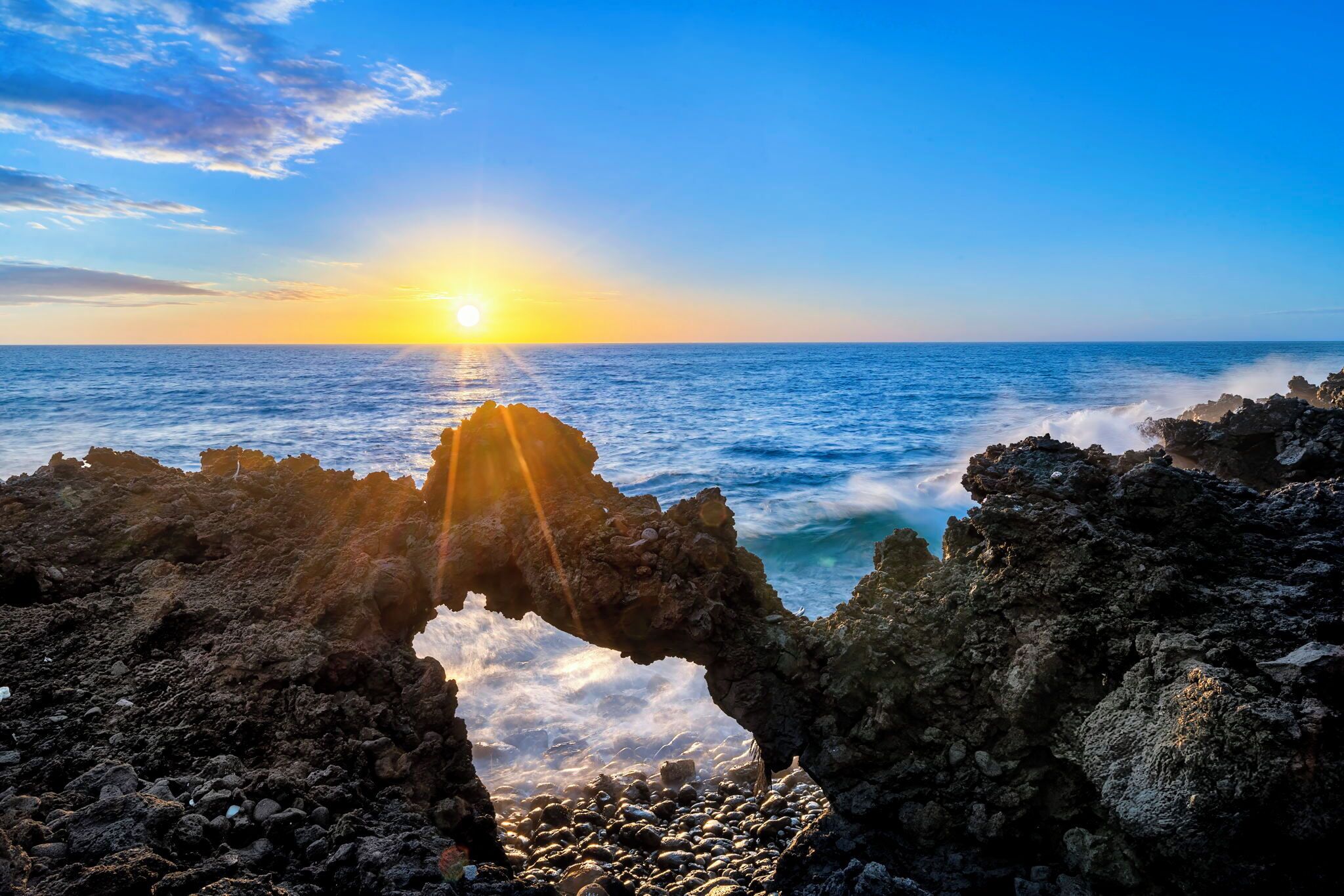 A natural rock formation with a sunlit view of the ocean.