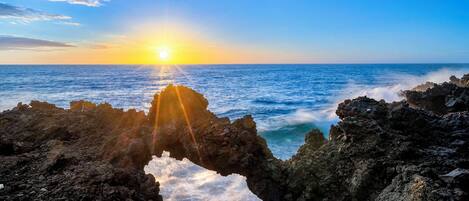 A natural rock formation with a sunlit view of the ocean.