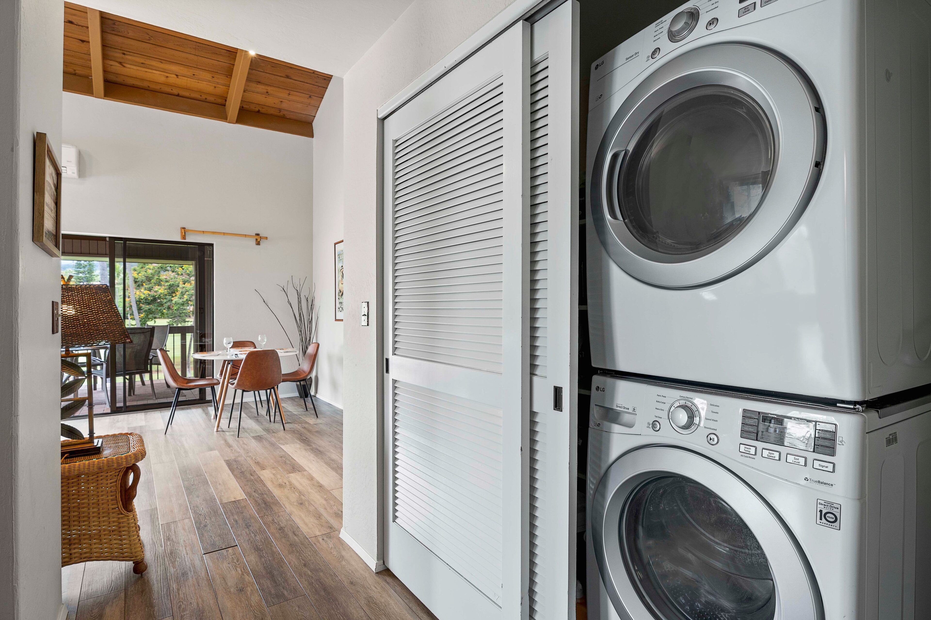A laundry room with stacked washing machines, a dining area with chairs and a table, and a view of the outdoors through a door.