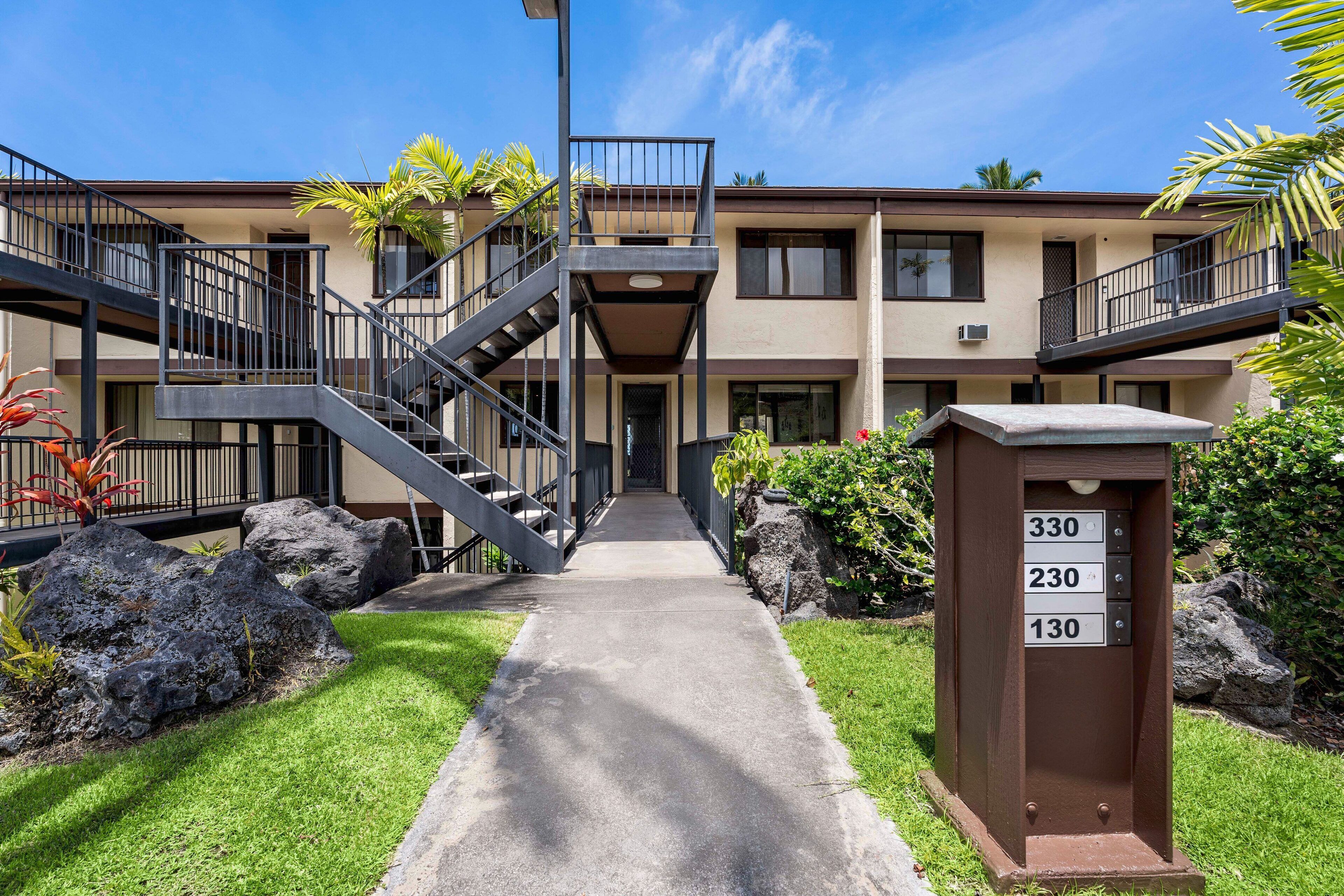 A multi-story building with a central staircase, a mailbox with apartment numbers, and a well-maintained lawn.