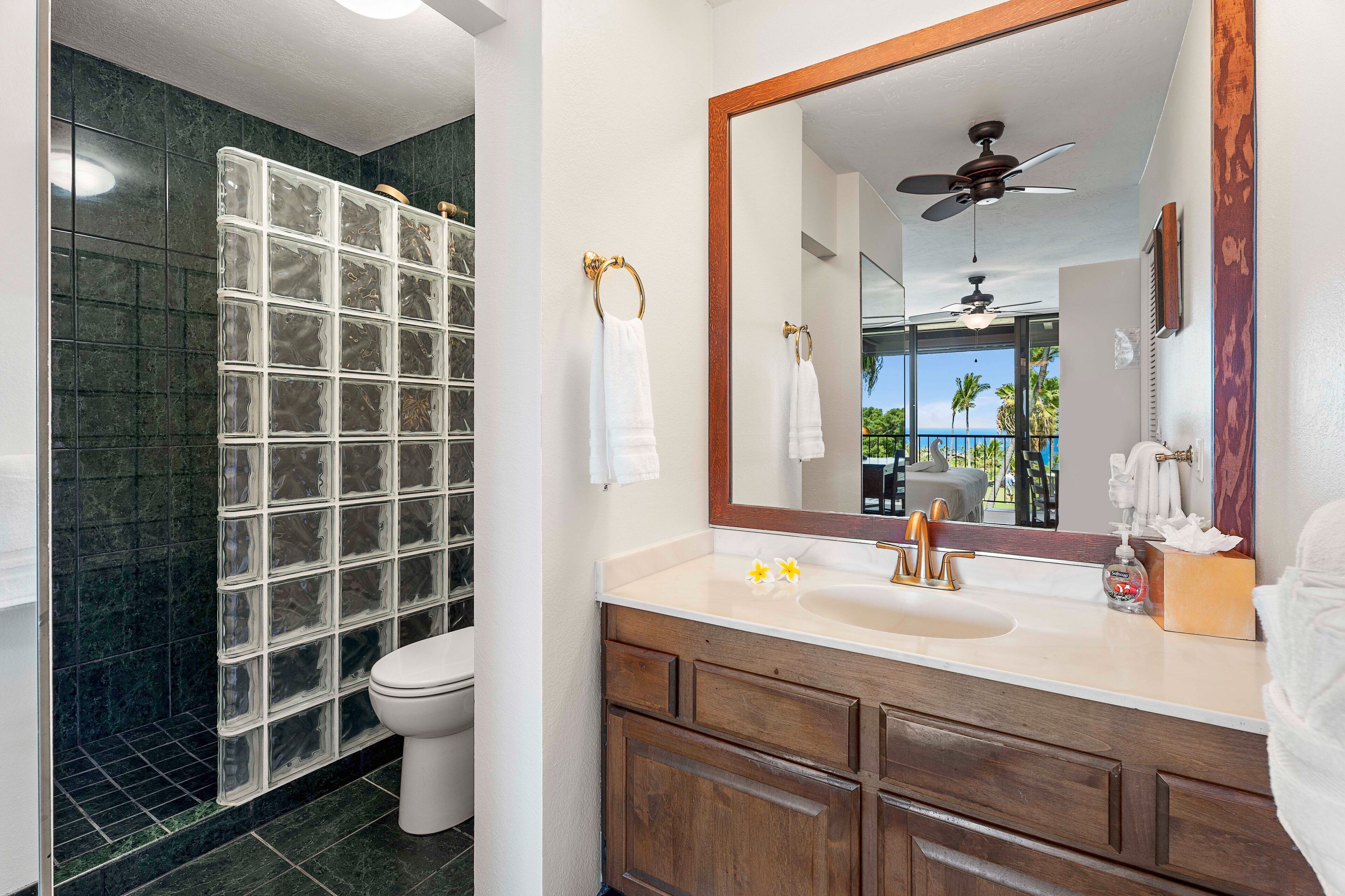 Une salle de bain dotée d’une douche à parois de verre, de toilettes blanches, d’un meuble-lavabo avec miroir et offrant une vue sur l’extérieur.