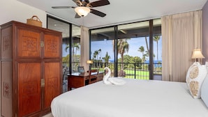 Hotelkamer met een groot bed, een houten kledingkast, een bureau met stoel en uitzicht op palmbomen door grote ramen.