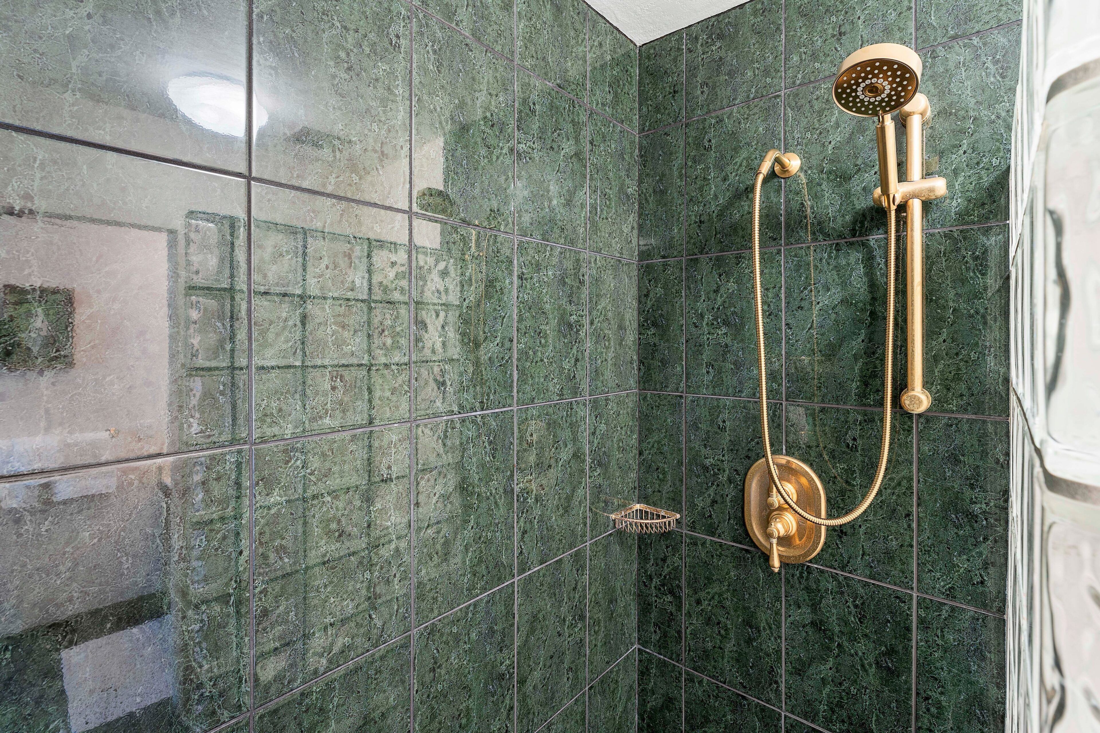 A shower with a gold showerhead and hose, set against a green marble wall.