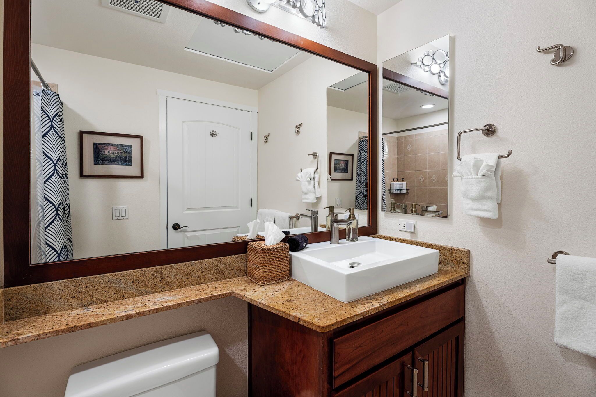 A bathroom with a white sink, wooden vanity, and a large mirror.