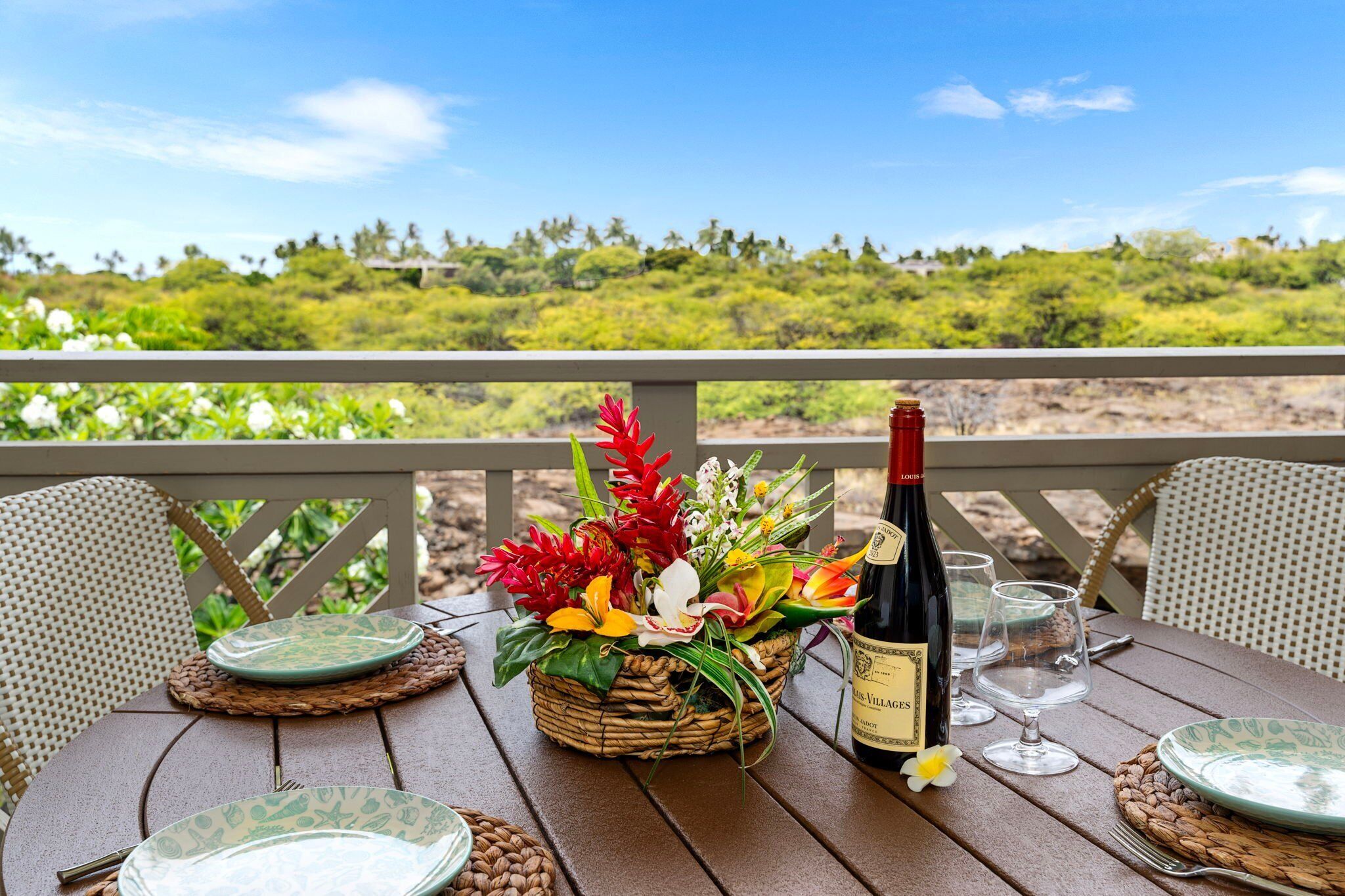 Une table dressée avec des assiettes, une bouteille de vin et un centre de table floral, sur un balcon donnant sur un paysage luxuriant.