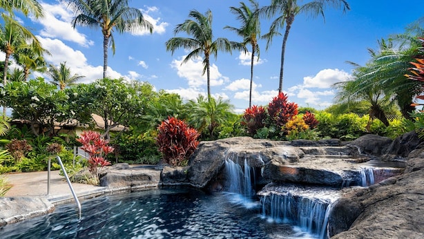 Ein tropisches Resort mit einem natürlichen Pool, tosenden Wasserfällen und üppiger Vegetation.