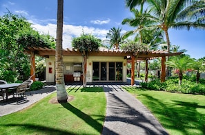A modern building with a covered patio, a lawn, and palm trees. - 2bed Lift with Concierge Onsite, Golf Course Views - Vrkcv (Kamuela)