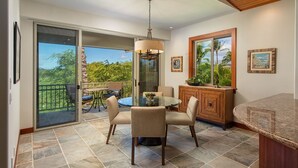 A dining area with a glass table and chairs, a wooden cabinet, and a view of a tropical garden through a large window.