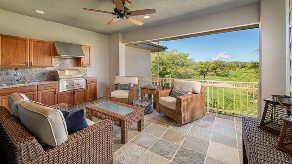 A spacious patio with wicker furniture, a kitchen area, and a view of a golf course. - Spacious Townhome - Stunning Golf Course Views - Pool & Fitness- Vrkcv (Kamuela)