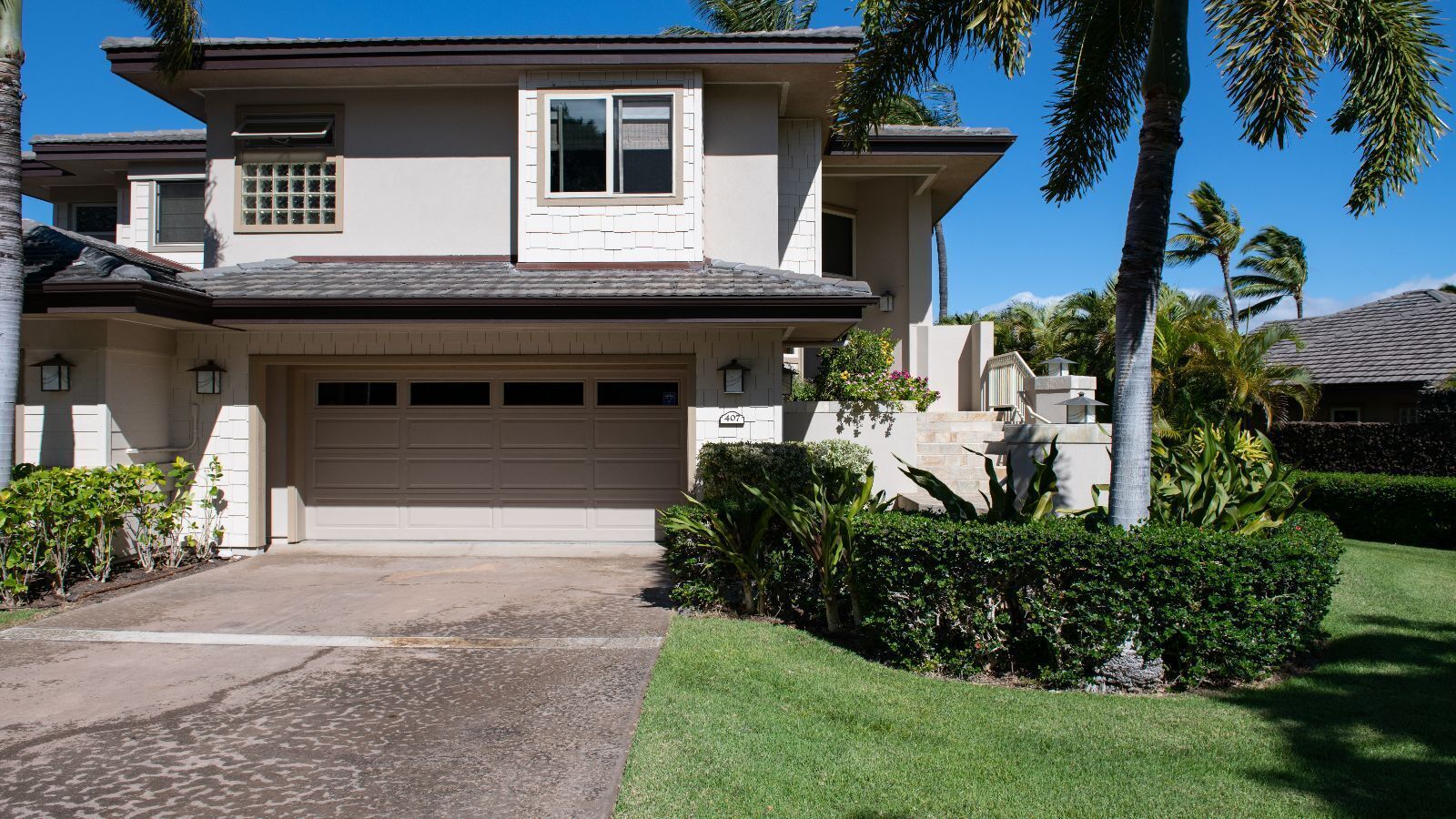 A two-story house with a garage, surrounded by well-maintained landscaping and palm trees.
