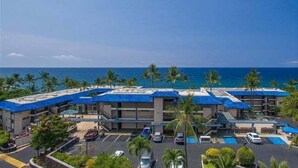A hotel with multiple buildings, a parking lot, and a view of the ocean. - Ocean Front - Walk to Kona Town! - Vrkcv (Kailua-Kona)
