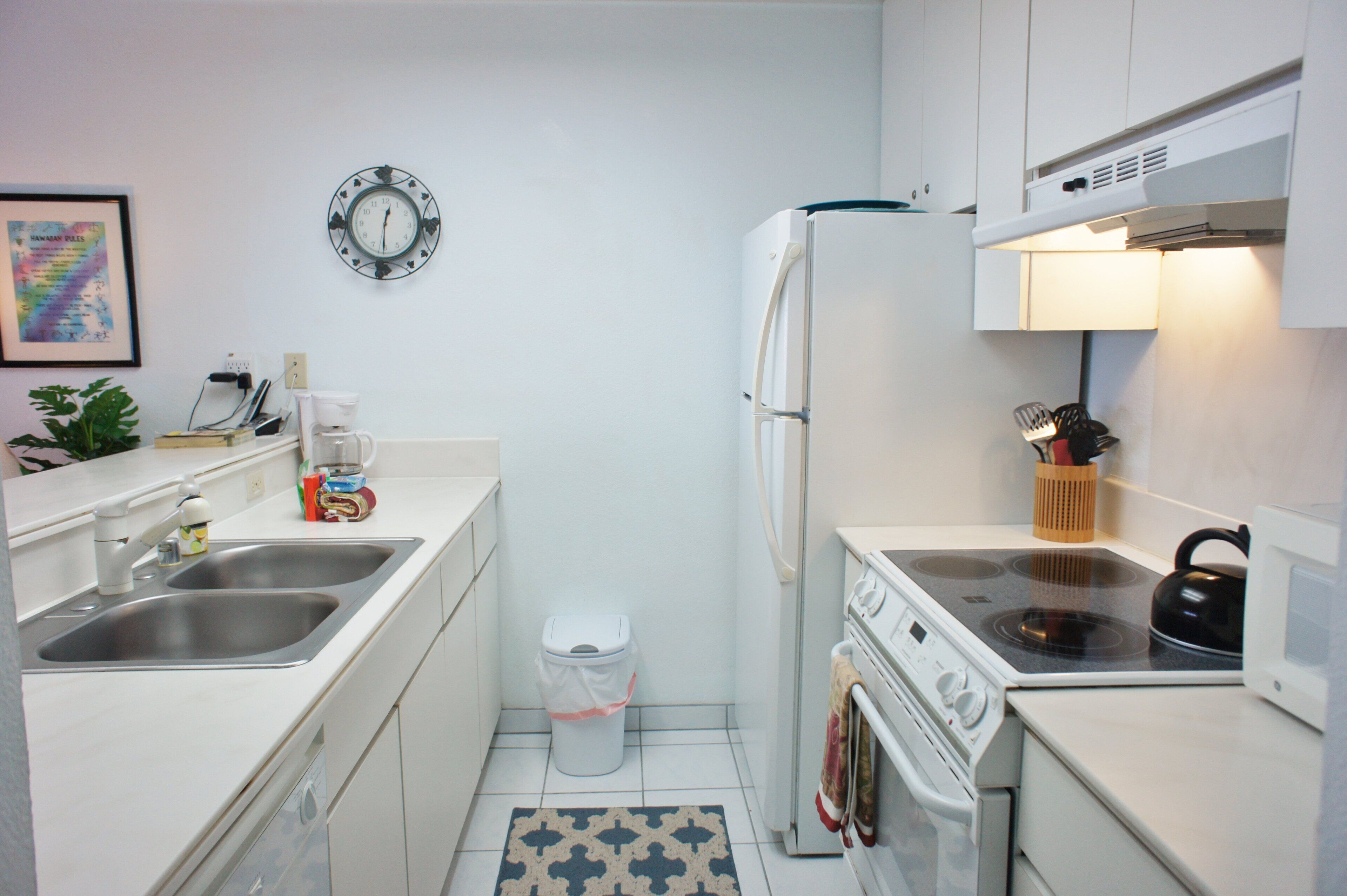 Una cocina compacta con armarios blancos, lavamanos de acero inoxidable, un microondas, un horno y una estufa a gas.