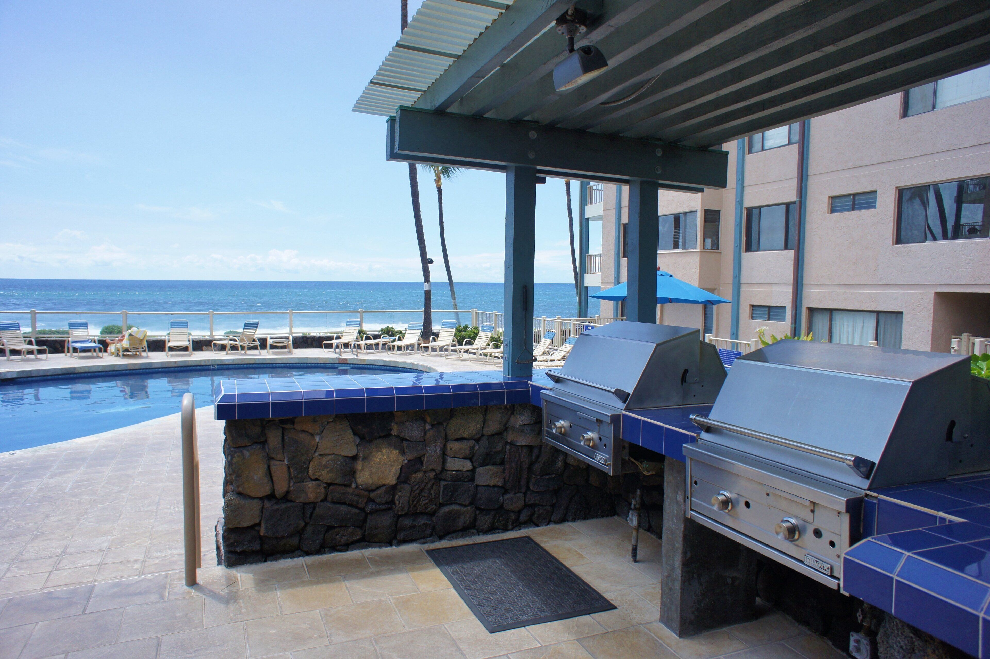 A poolside area with a stone wall, a grill, and lounge chairs.