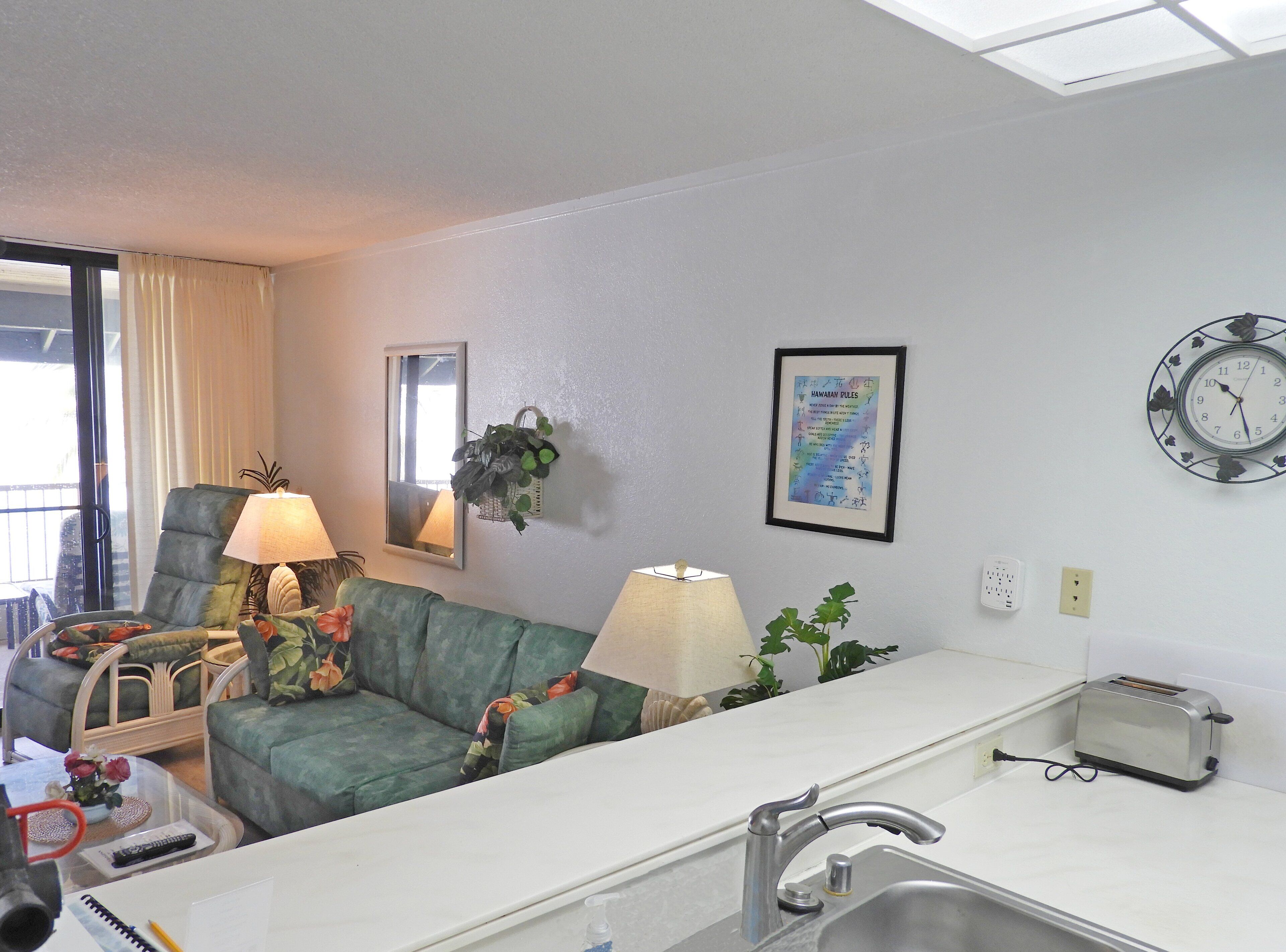 A compact hotel room with a kitchenette, a sofa, a dining table, and a window with curtains.