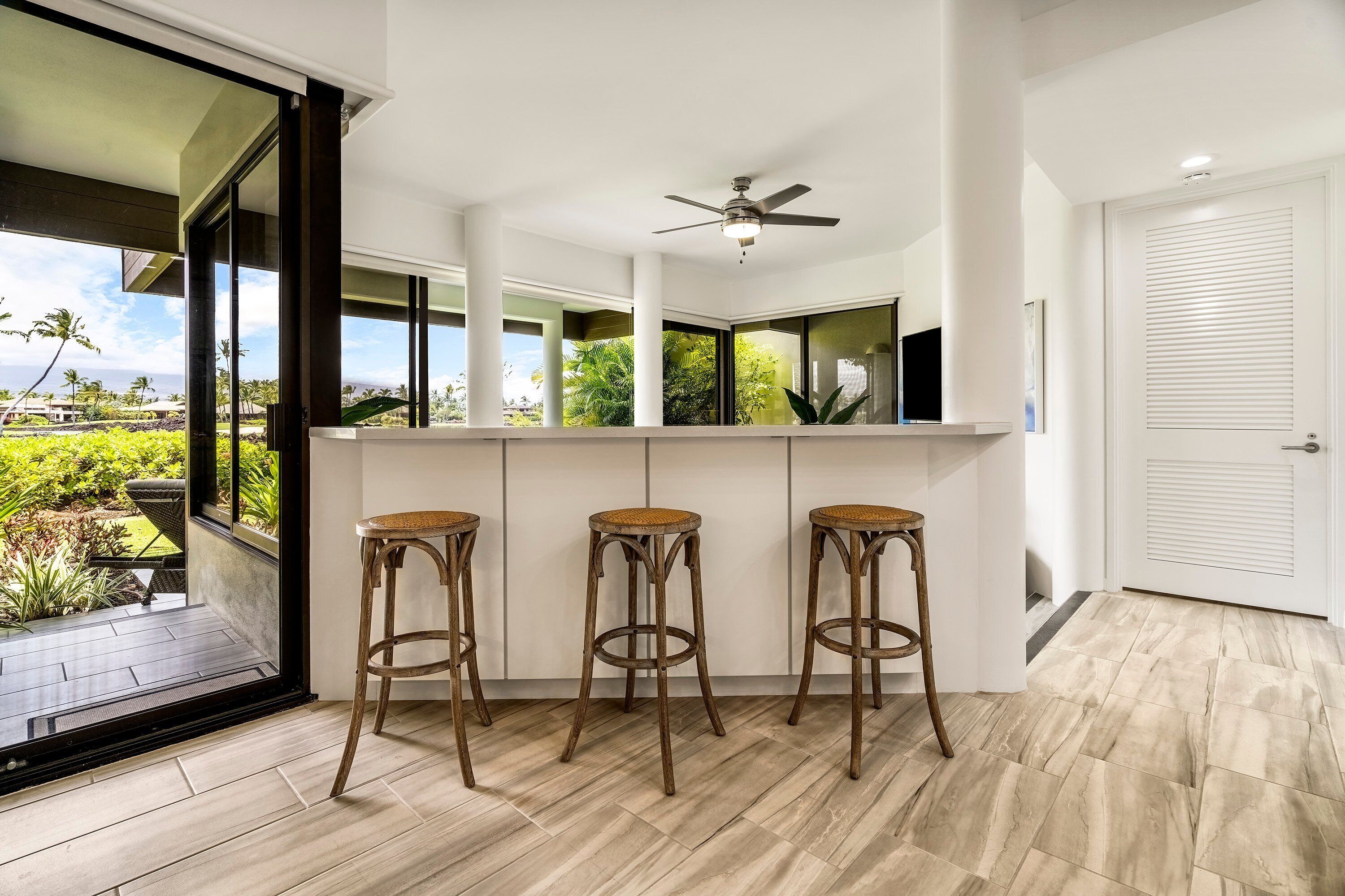 A modern kitchen with a bar area, large windows, and a ceiling fan.