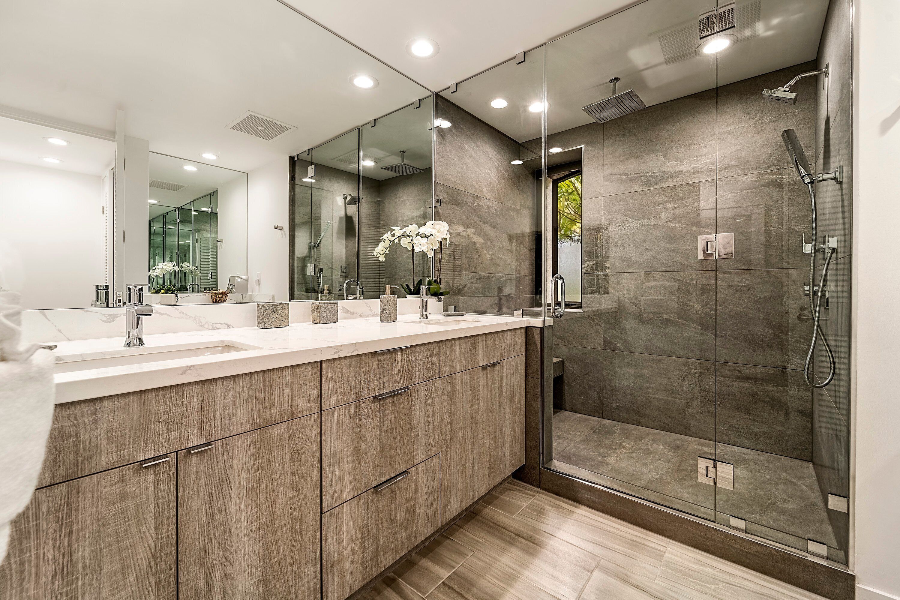 A modern bathroom with a large mirror, a walk-in shower, and a wooden vanity.