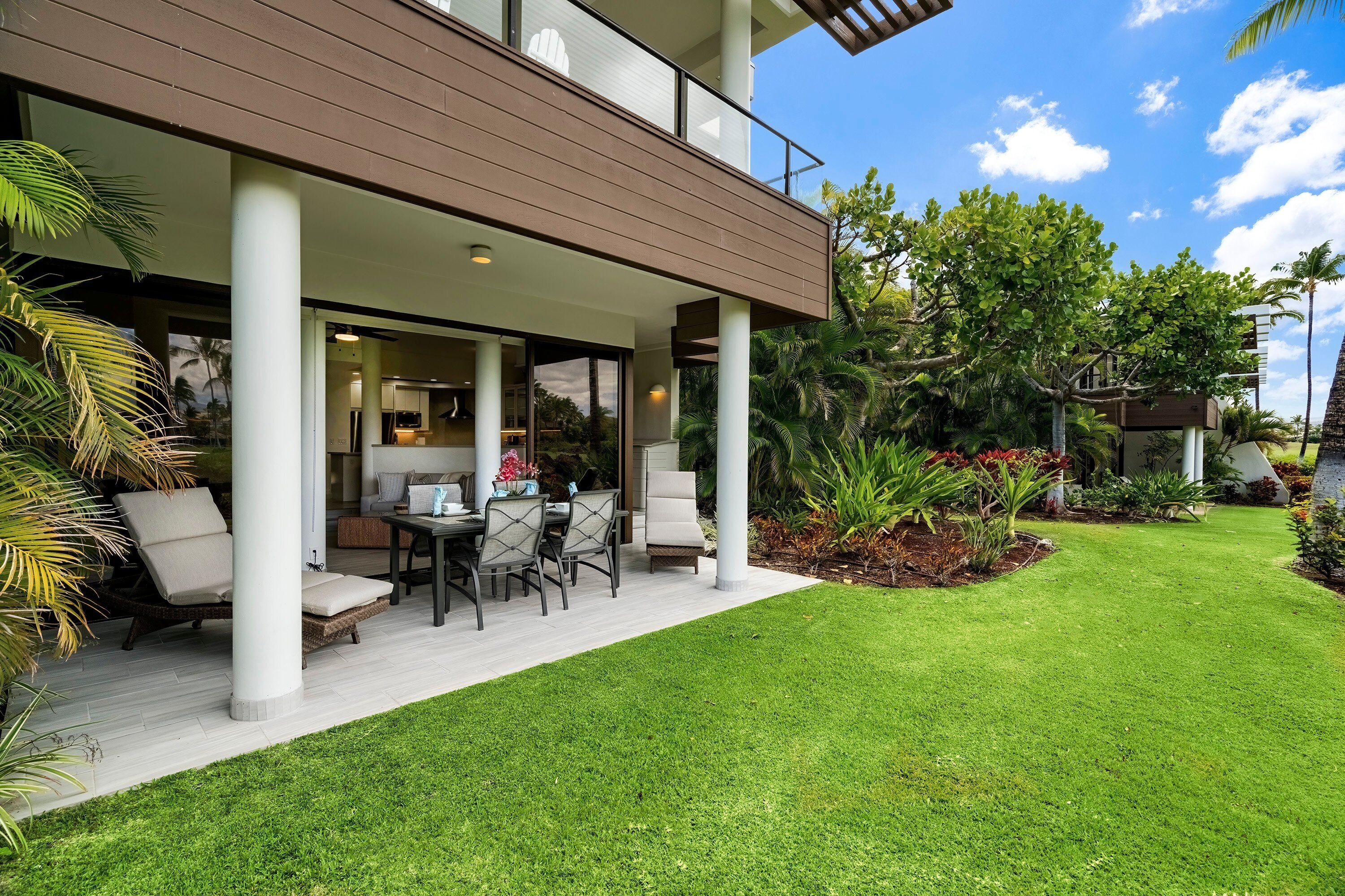 A modern house with a covered patio, outdoor seating, and lush greenery.