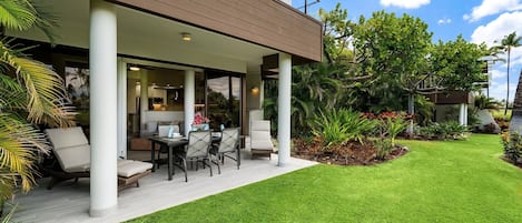 A modern house with a covered patio, outdoor seating, and lush greenery.