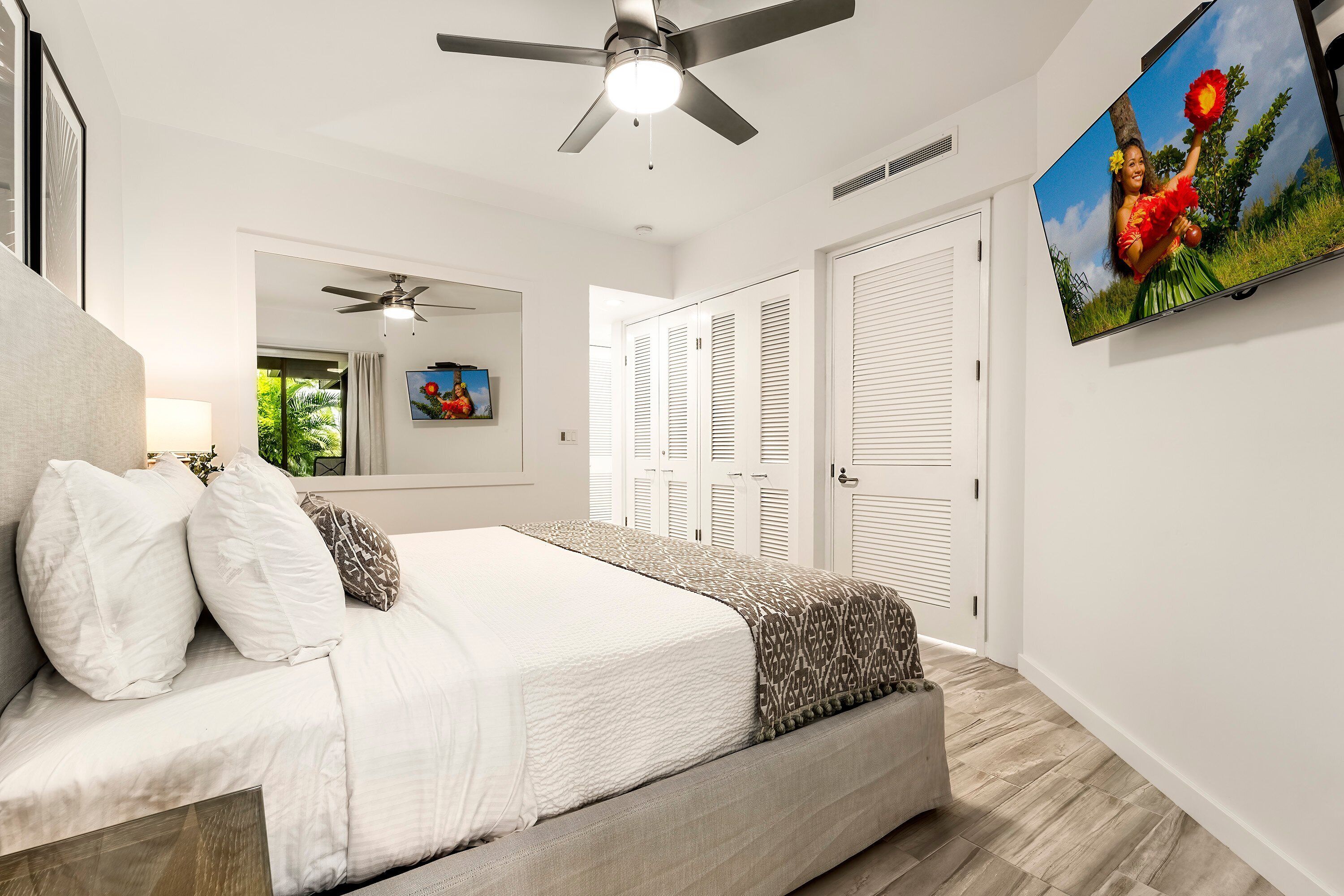 A bedroom with a bed, a ceiling fan, a TV, and a door with shutters.