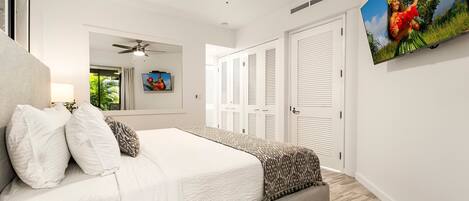 A bedroom with a bed, a ceiling fan, a TV, and a door with shutters.