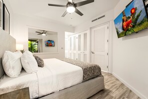 Une chambre à coucher avec un lit, un ventilateur de plafond, une télévision et une porte avec des volets.