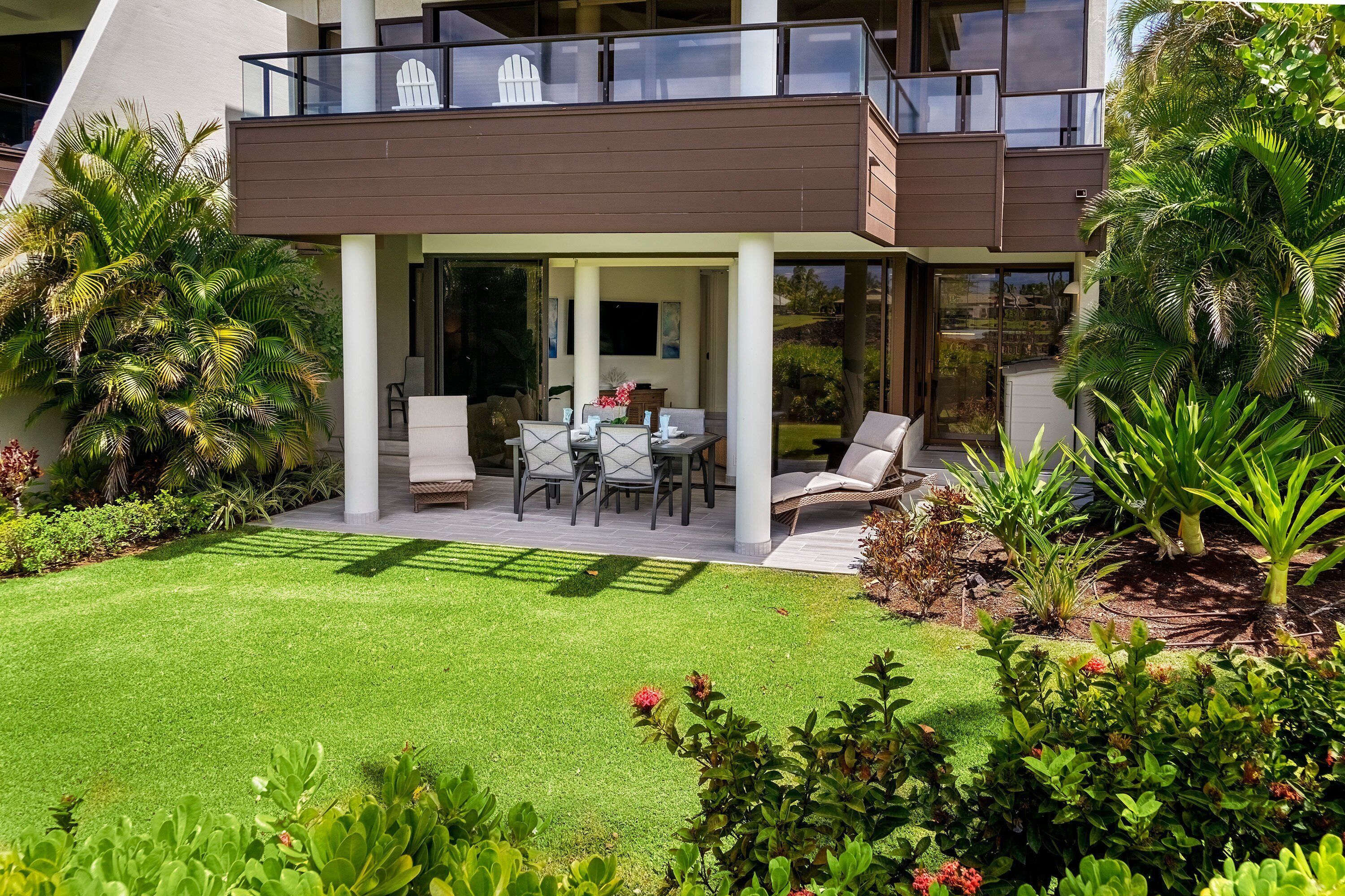 A modern two-story house with a covered patio, outdoor seating, and lush landscaping.