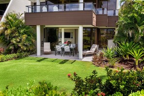 Une maison moderne à deux étages dotée d’un patio couvert, d’un espace salon extérieur et d’un aménagement paysager luxuriant.