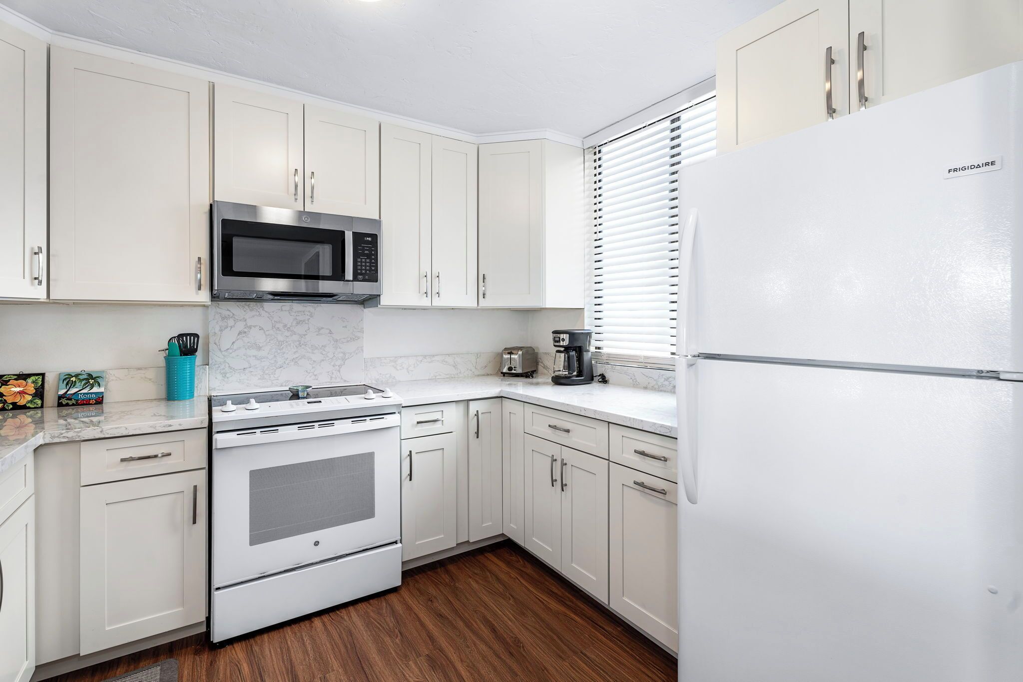 Una cocina moderna con armarios blancos, un microondas de acero inoxidable, un horno empotrado y un refrigerador.