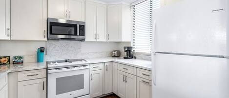 Una cocina moderna con armarios blancos, un microondas de acero inoxidable, un horno empotrado y un refrigerador.