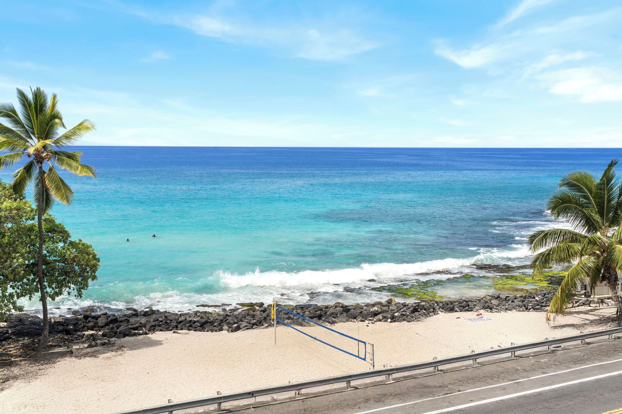 Een strand met helder turquoise water, een zandstrand en palmbomen.