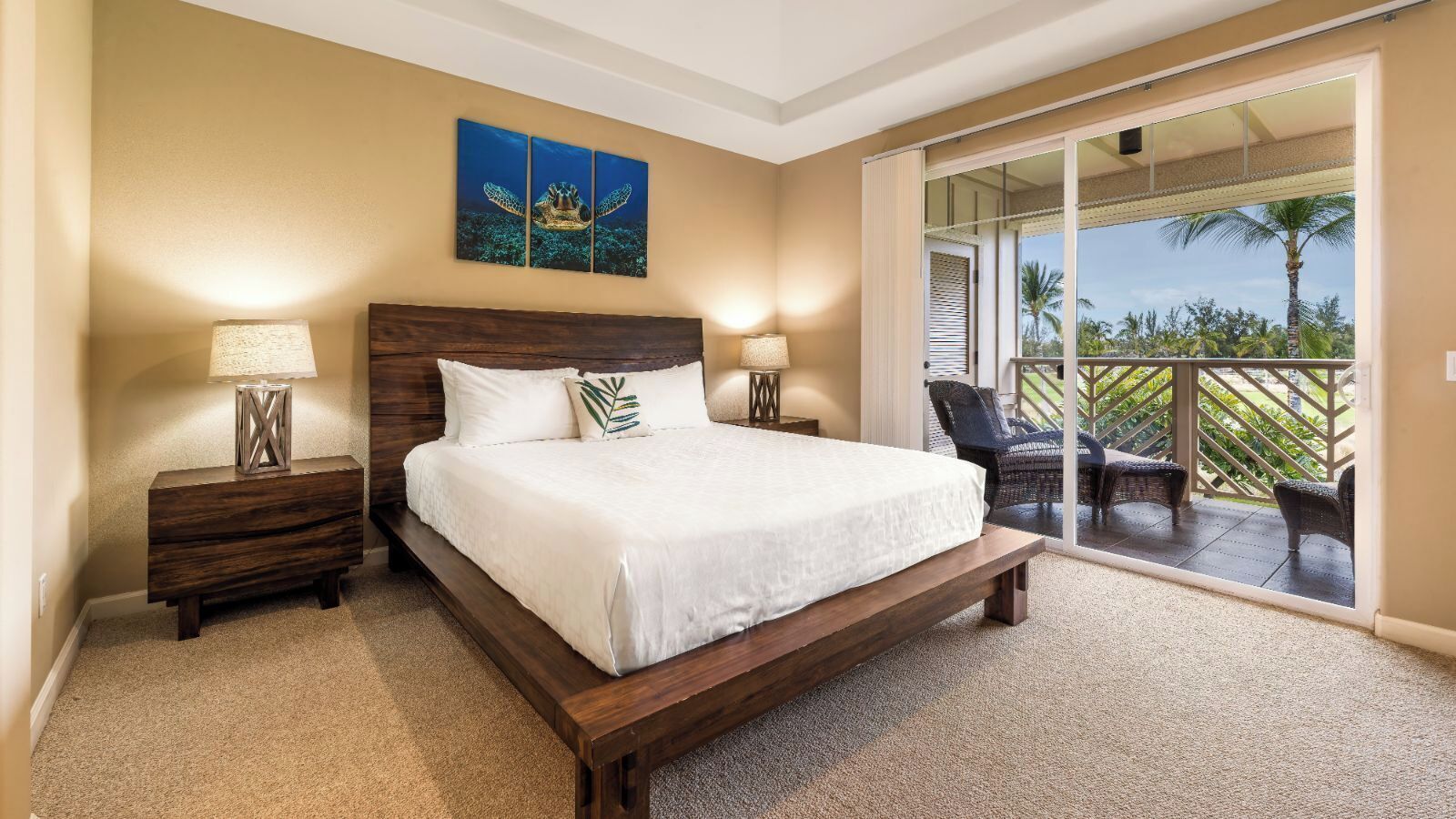 A bedroom with a large bed, two bedside tables, a ceiling light, and a view of a balcony with outdoor furniture.