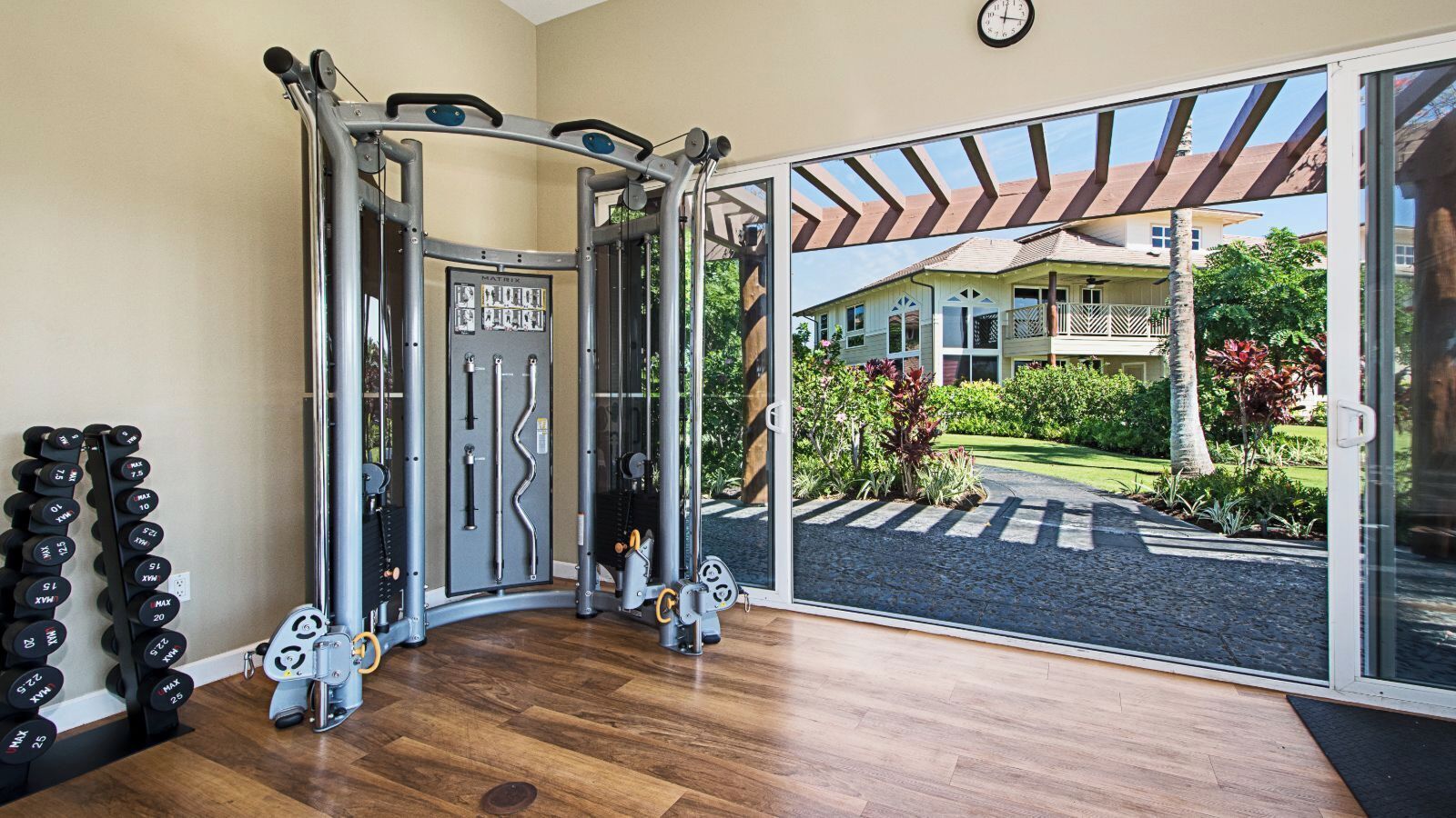 A gym with a variety of exercise equipment, including a squat rack and dumbbells, and a view of a house through a glass door.