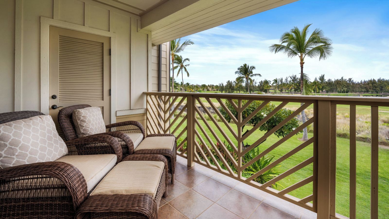 A balcony with wicker furniture, a view of a golf course, and a palm tree.