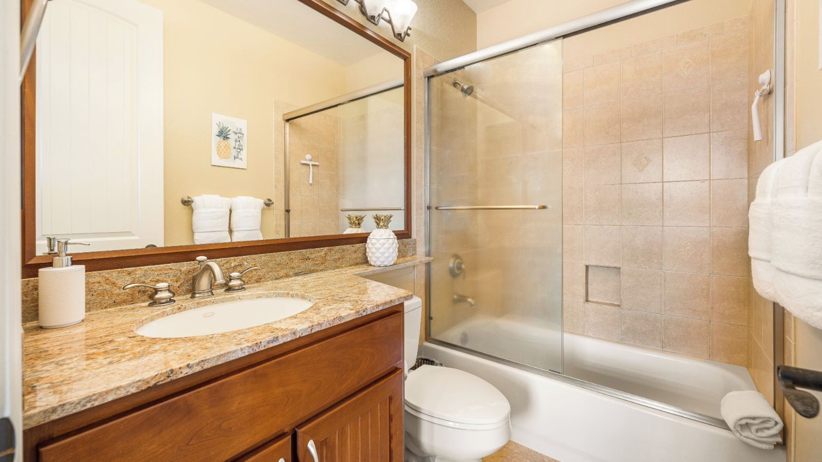 A bathroom with a granite countertop, a white sink, a toilet, and a glass-enclosed shower.