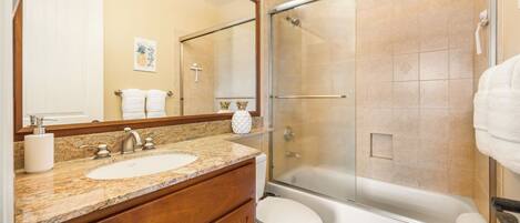 A bathroom with a granite countertop, a white sink, a toilet, and a glass-enclosed shower.
