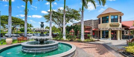 A fountain surrounded by palm trees and a building with a sign that reads "Hotel".