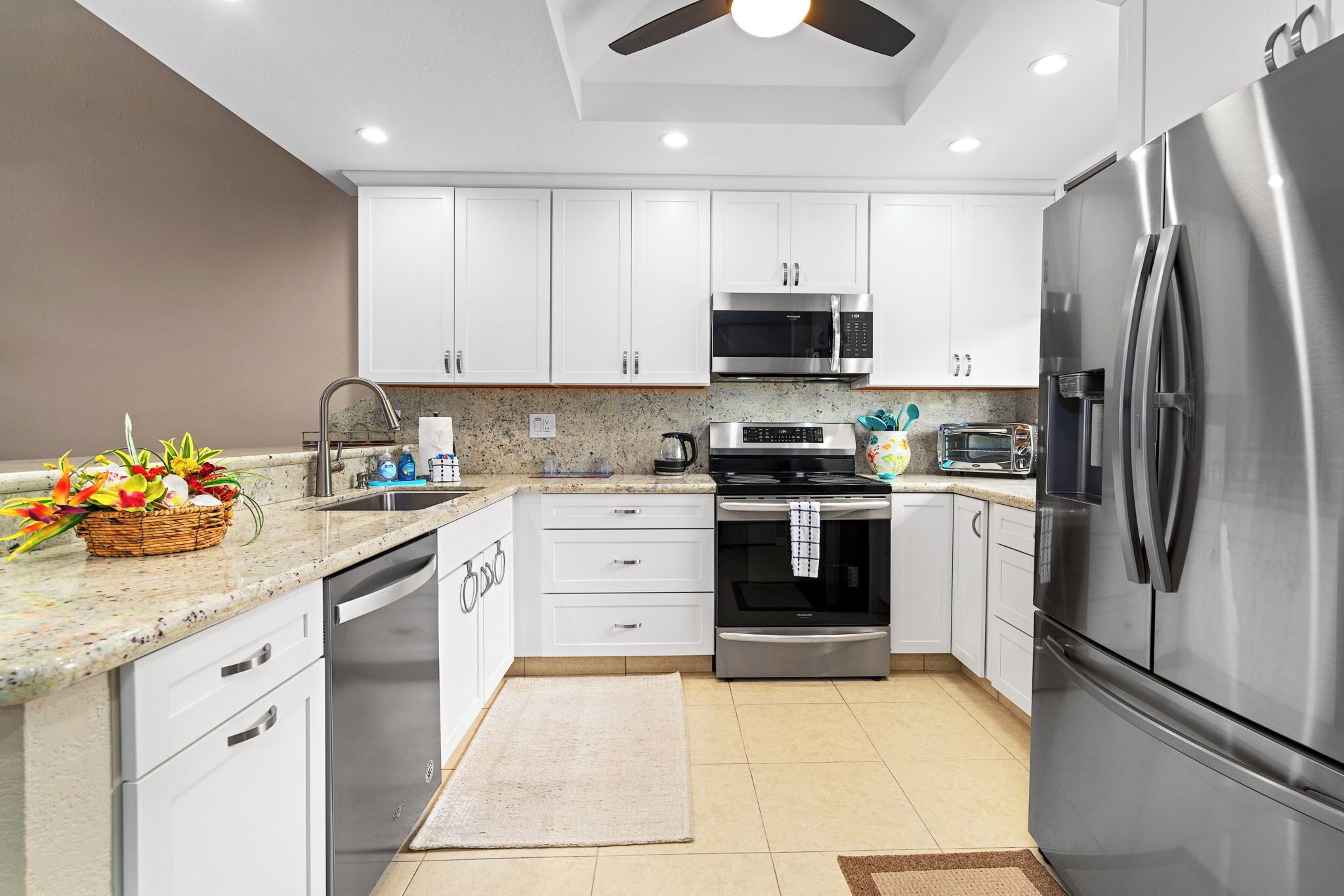 A modern kitchen with white cabinets, stainless steel appliances, a granite countertop, and a ceiling fan.