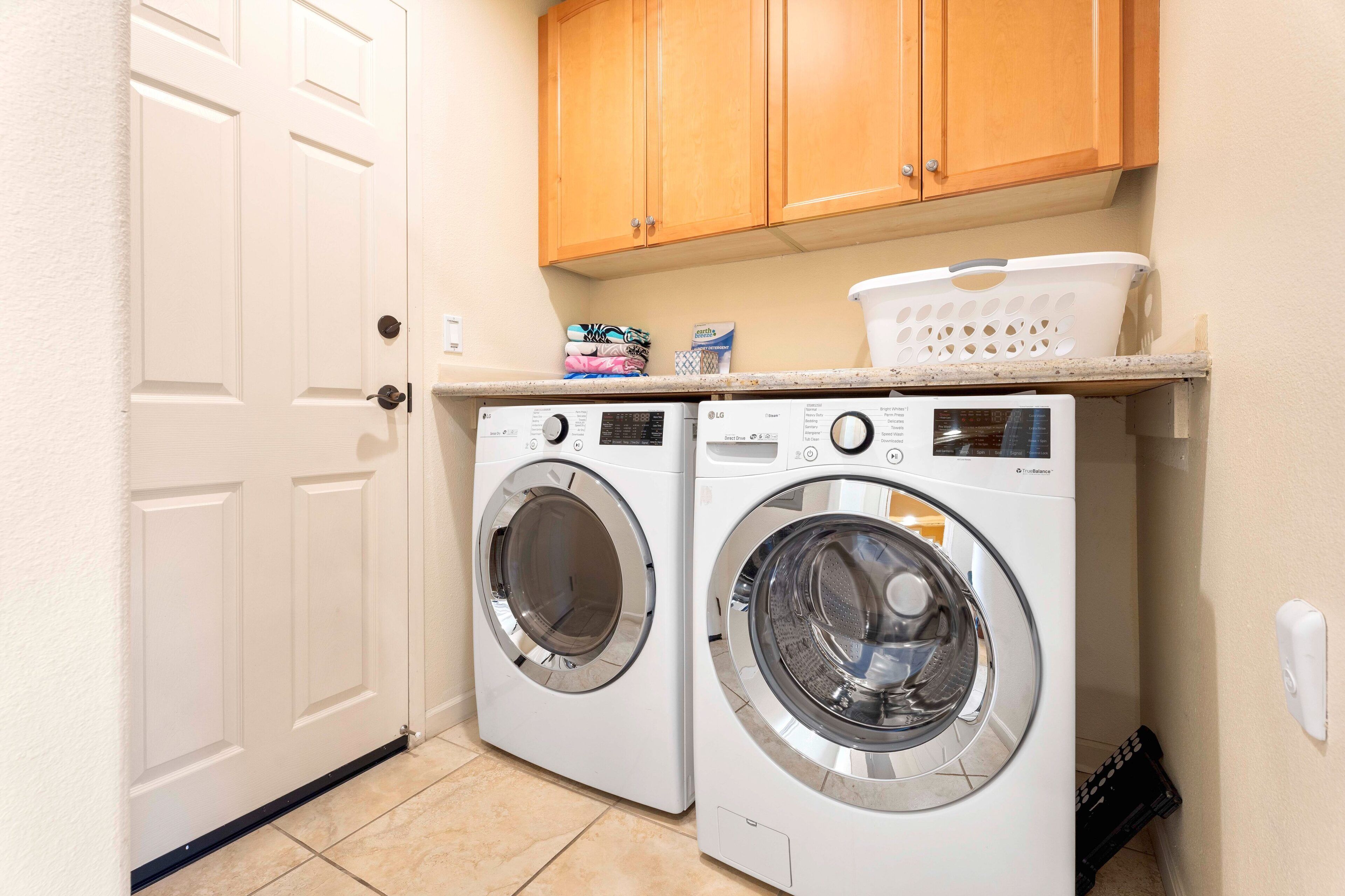 A laundry area with two front-loading washing machines, wooden cabinets above, and a laundry basket on the countertop.