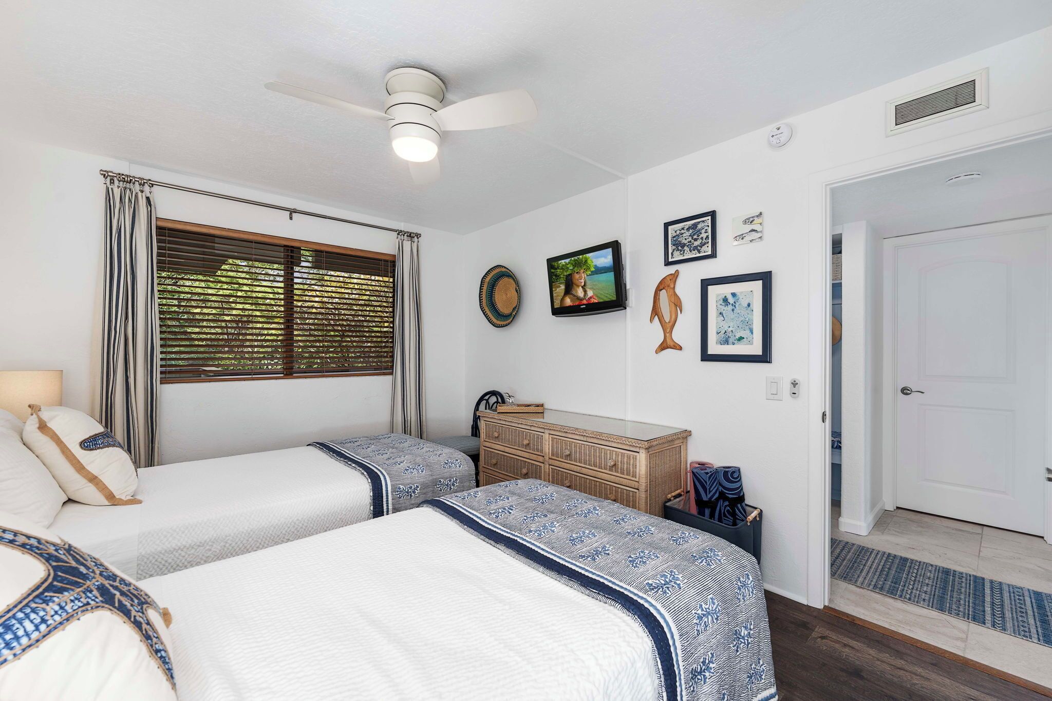 A hotel room with two beds, a ceiling fan, a TV, and a wooden dresser.