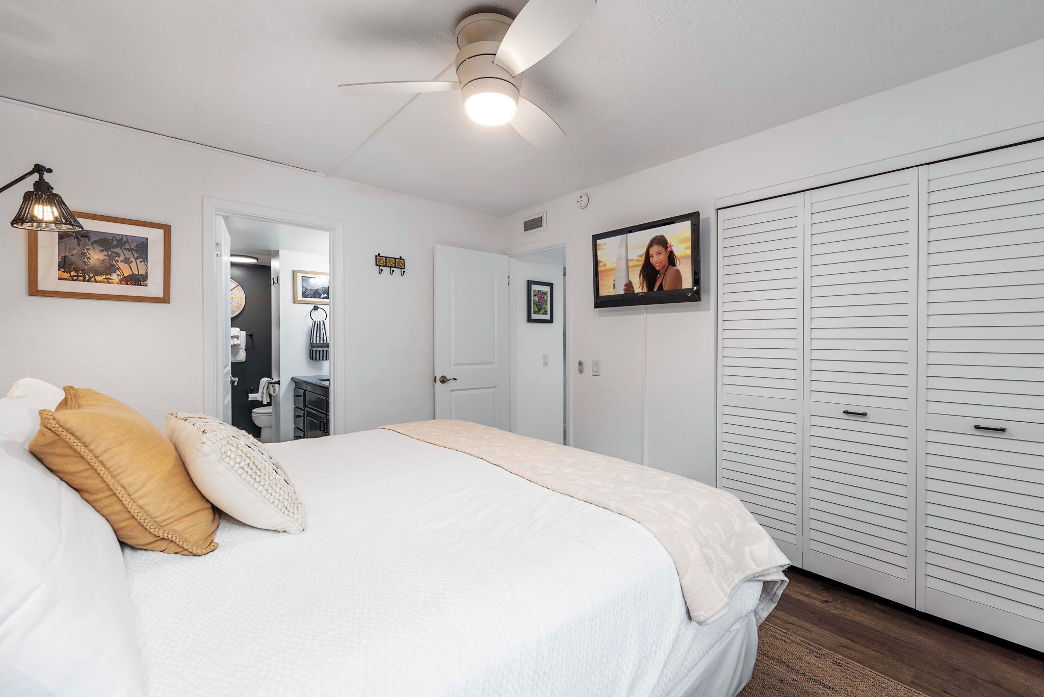 A bedroom with a bed, a ceiling fan, a wardrobe, and a door leading to a bathroom.