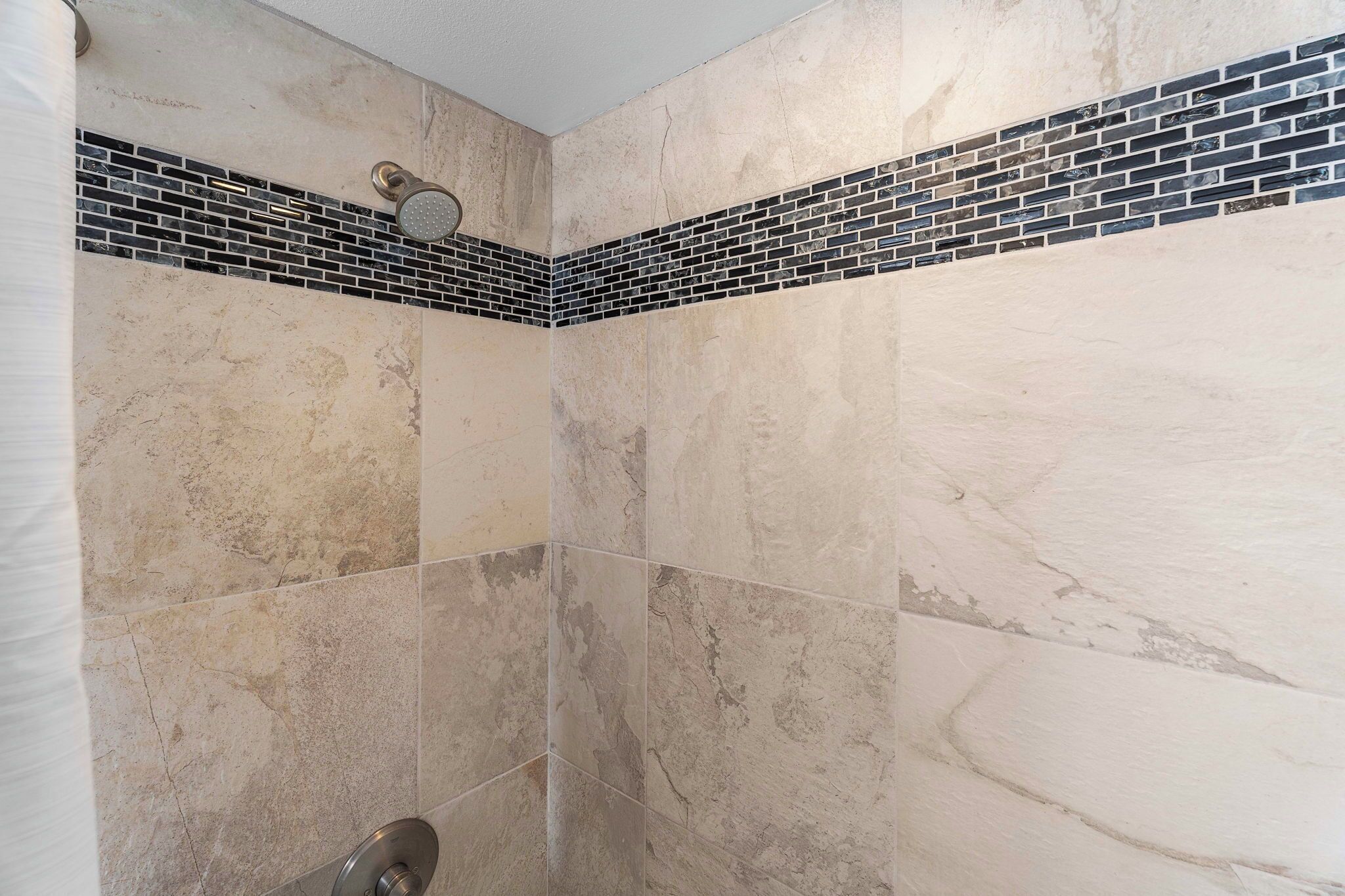A shower with beige tiles and a black and white mosaic border.
