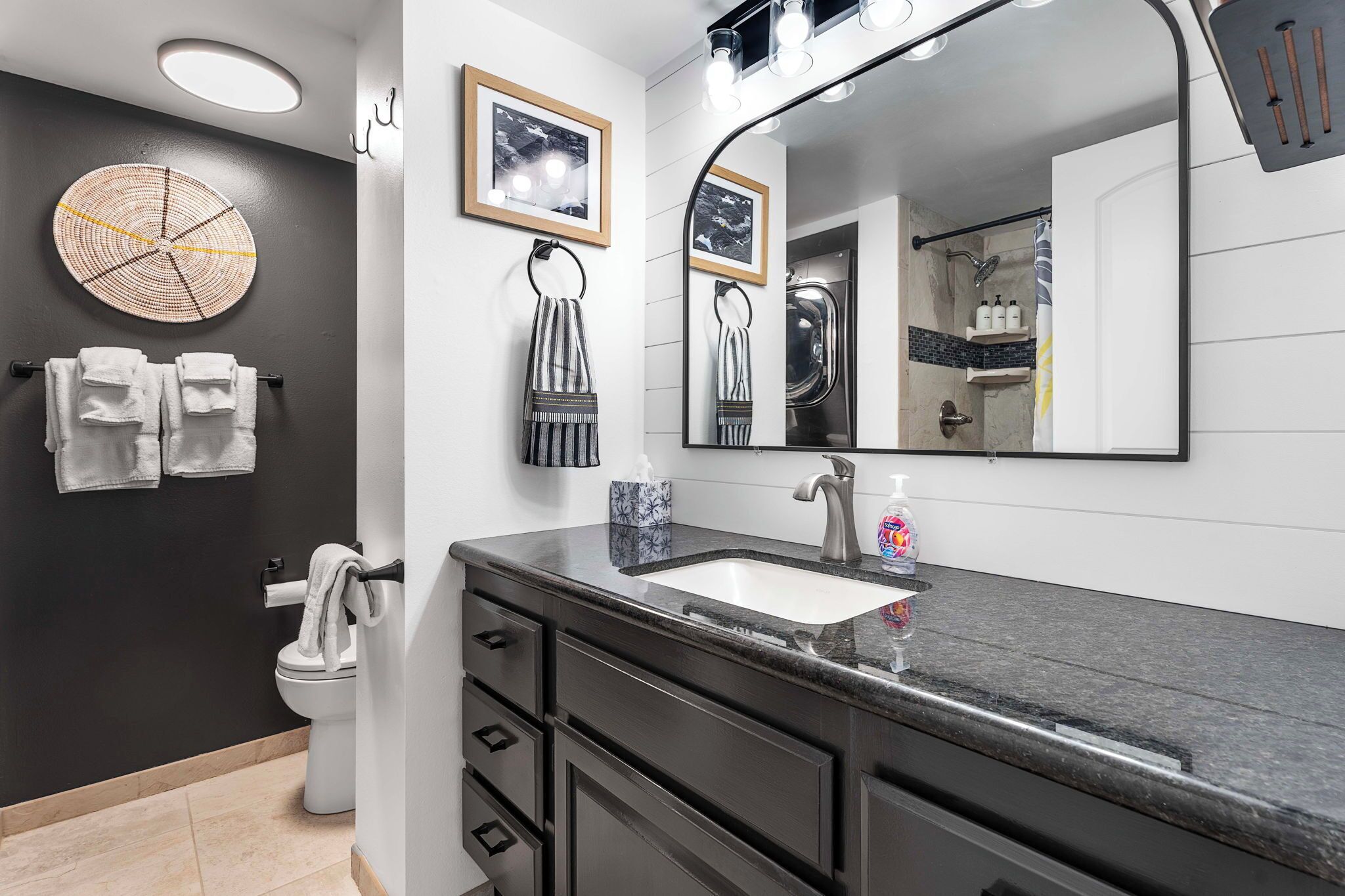 A modern bathroom with a large mirror, a sink, and a toilet. There are towels and toiletries on the counter.